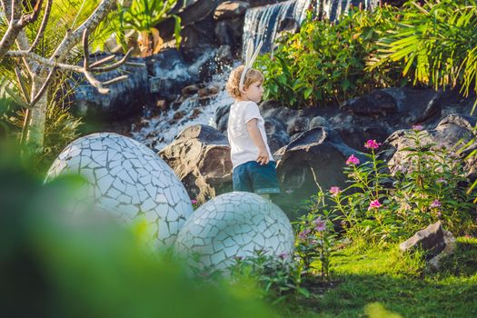 Cute little kid boy with bunny ears having fun with traditional Easter eggs hunt, outdoors. Celebrating Easter holiday. Toddler finding, colorful eggs.