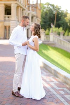 Happy young bride and groom holding hands and standing outdoors. Concept of relationship, wedding and bridal photo session.