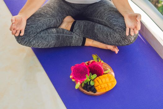 hand of a woman meditating in a yoga pose, sitting in lotus with fruits in front of her dragon fruit, mango and mulberry.