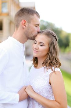 European groom kissing bride and holding hands outdoors. Concept of wedding and bridal photo session, relationship.