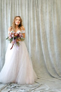 Young bride standing at studio with flowers. Concept of wedding and bridal photo sesion, fashion.