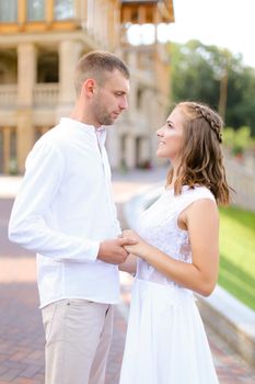 Happy bride and groom holding hands and standing outdoors. Concept of relationship, wedding and bridal photo session.