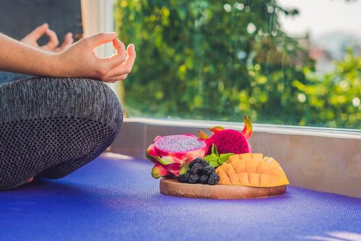 hand of a woman meditating in a yoga pose, sitting in lotus with fruits in front of her dragon fruit, mango and mulberry.