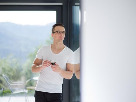 young handsome man drinking morning coffee by the window in his home