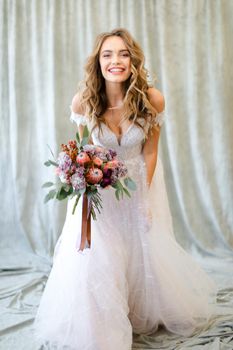 Young caucasian bride standing at studio with flowers. Concept of wedding and bridal photo sesion, fashion.