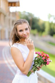 Young caucasian bride wearing white dress and standing outside with flowers. Concept of wedding and bridal photo session, floristic art.