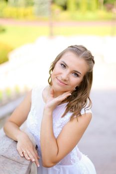 Happy bride wearing white dress standing outside and smiling. Concept of bridal photo session and wedding, nice fiancee.