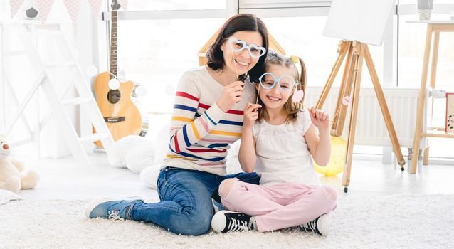 Pretty mother and daughter playing with stick lips and glasses