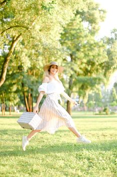 Young woman jumping in park and running, wearing fashionable clothes and hat. Concept of summer sales and style.