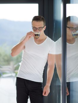 young handsome man drinking morning coffee by the window in his home