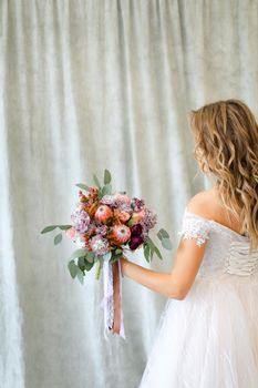 Back view of young caucasian bride standing at studio with flowers. Concept of wedding and bridal photo sesion, fashion.