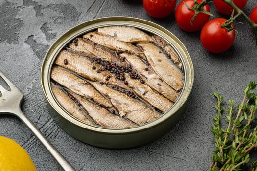 Smoked canned sprats in cooking oil in open tin can set, on gray stone table background