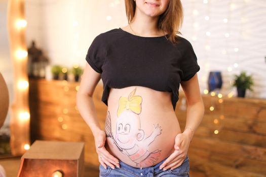 Young pregnnant woman with painted belly at home. Concept of maternity and pregnance.