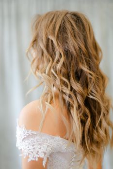 Back view of bride with long curly hair at studio. Concept of bridal photo session and cute hair do for fiancee.