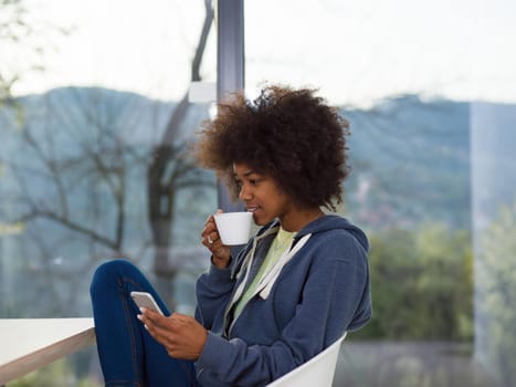 Handsome young african american woman drinking coffee and using a mobile phone at  home