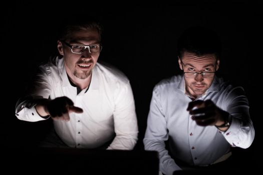 close up.two colleagues sitting at their Desk and pointing at you.isolated on black