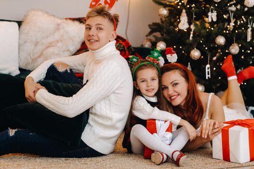 a happy family is lying on the floor of the house with New Year's gifts, next to the Christmas tree,