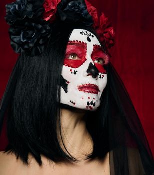 portrait of a beautiful woman with a sugar skull makeup with a wreath of flowers on her head, red background