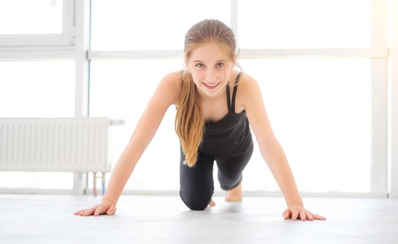 Pretty young girl doing exercises on a floor in white room and lookig into the camera