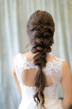 Back view of brunette fiancee with braid hair at studio. Concepf of bridal hair do and wedding.
