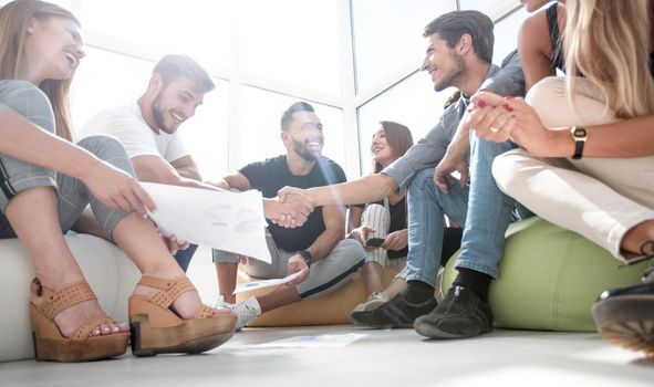 friends shaking hands, sitting on the floor in the new office. the concept of a startup