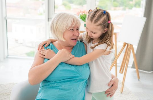 Cute little girl embracing smiling granny in light room