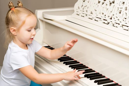 A nice little girl is playing on a big white piano. The concept of musical and aesthetic education of a child.