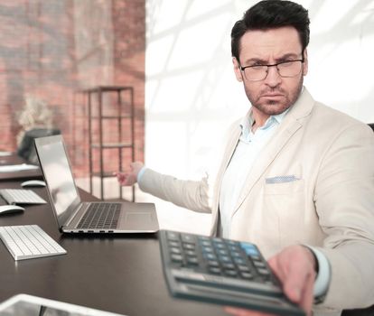 behind the glass.serious businessman with calculator sitting at his Desk. photo with copy space