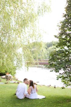 Young couple sittling near lake on grass and kissing. Concept of relationships, youth and love.