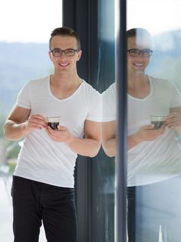 young handsome man drinking morning coffee by the window in his home