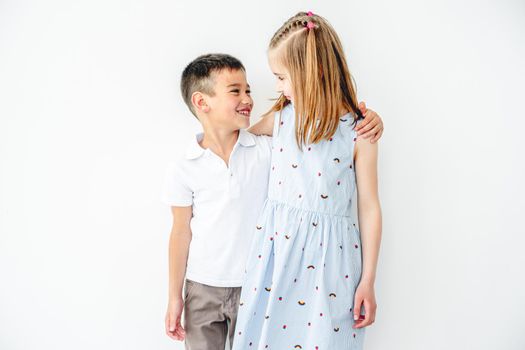 Smiling boy and girl kids hugging on white wall background