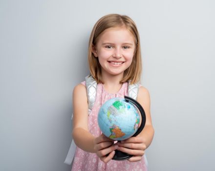 Schoolgirl holding small globe in front of her on gray background