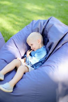 Little male child sitting in bag chair on grass. Concept of childhood.