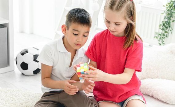 Cute girl and boy kids solving with rubik's cube in light room