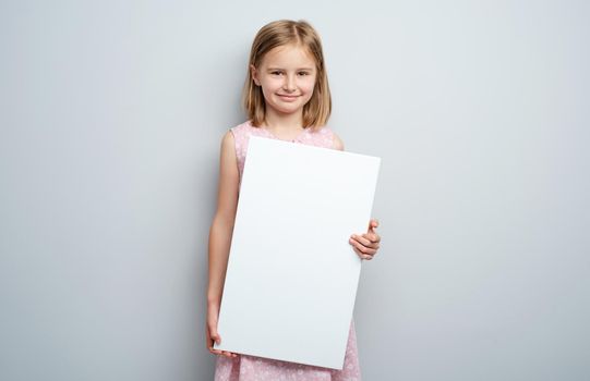 Little girl holding vertical empty placard on gray wall background