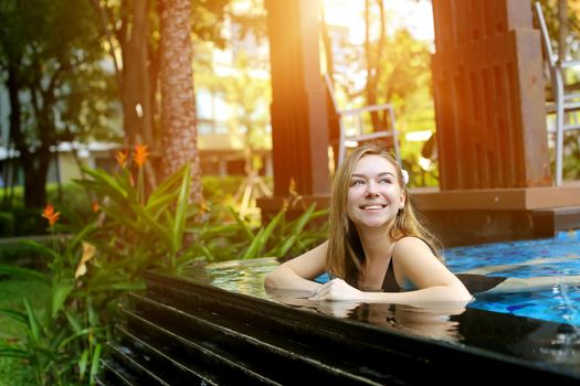 young woman swimming in tropical pool in thailand. female look up and smile, enjoys endless summer in tropical summer. concept of travel