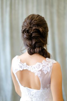 Back view of brunette bride with braid hair at studio. Concepf of bridal hair do and wedding.