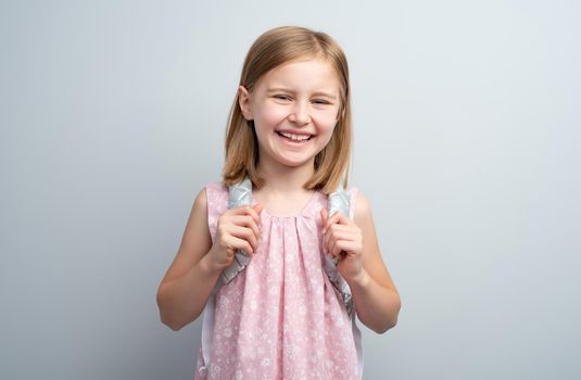Smiling school girl with backpack on gray background