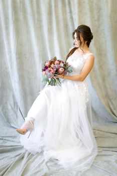 Caucasian bride sitting at photo studio with bouquet of flowers. Concept of wedding and fianceee fashion.