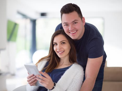 Young couple using tablet computer at luxury home together, looking at screen, smiling.