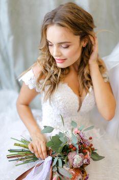 Blonde bride with bouquet of flowers sitting at studio. Concept of bridal make up, photo session and wedding.