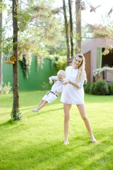 Young european mom walking with child on grass in yard. Concept of motherhood and kids, summer season.