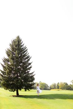 Young american couple walking near green big spruce on grass in white sky background. Concept of evergreens and wedding.