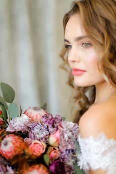 Close up portrait of young bride with bouquet of flowers at studio. Concept of floristic art, beauty and beautiful wedding photo session.