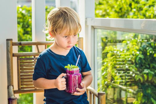 The boy holds smoothies from a dragon fruit with a mint leaf and a drinking straw.