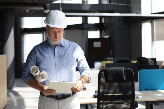 Thoughtful mature architect wearing hardhat in casual wear inspects new modern building