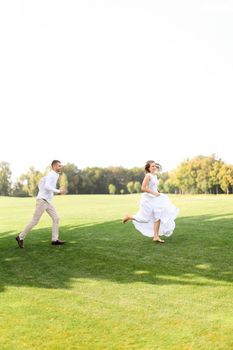 Groom and young bride running and playing on grass. Concept of wedding photo session on open air and nature.