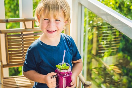 The boy holds smoothies from a dragon fruit with a mint leaf and a drinking straw.