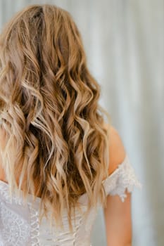 Back view of bride with long blonde curly hair at studio. Concept of bridal photo session and cute hair do for fiancee.