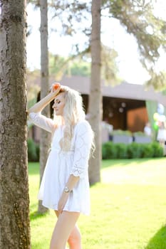 Young blonde caucasian woman standing near tree in white shirt. Concept of female person, nature and summer